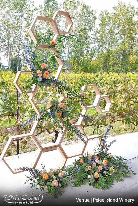 A tall organic wooden arch made up of an asymmetric orientation of hexagons, with wild overflowing installments of flowers in peach orange and blue.